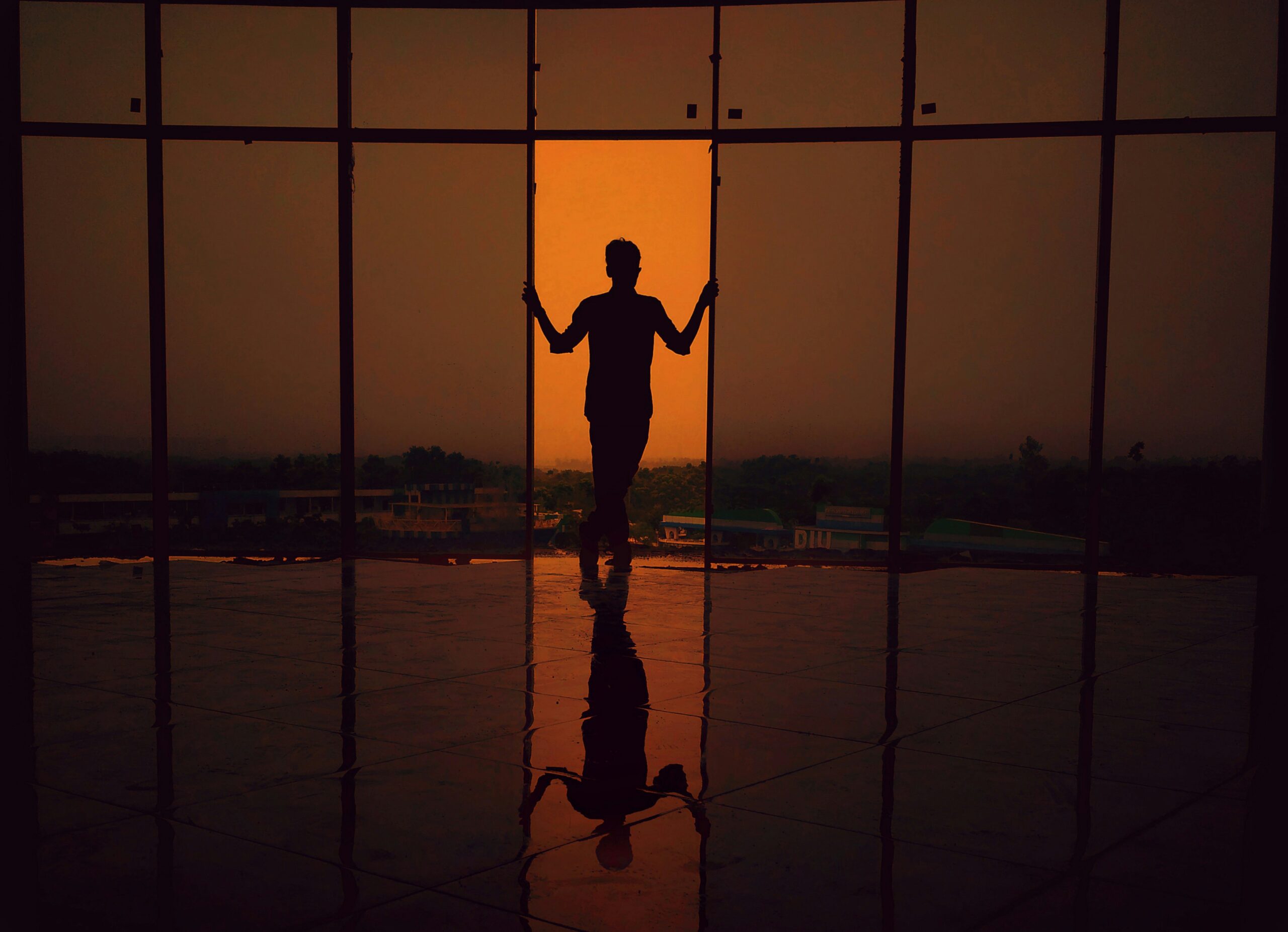DX-ROI Silhouette of a person standing by large windows at sunset, their reflection visible on a shiny floor—capturing the quiet elegance perfect for a website footer or stylish footer section.